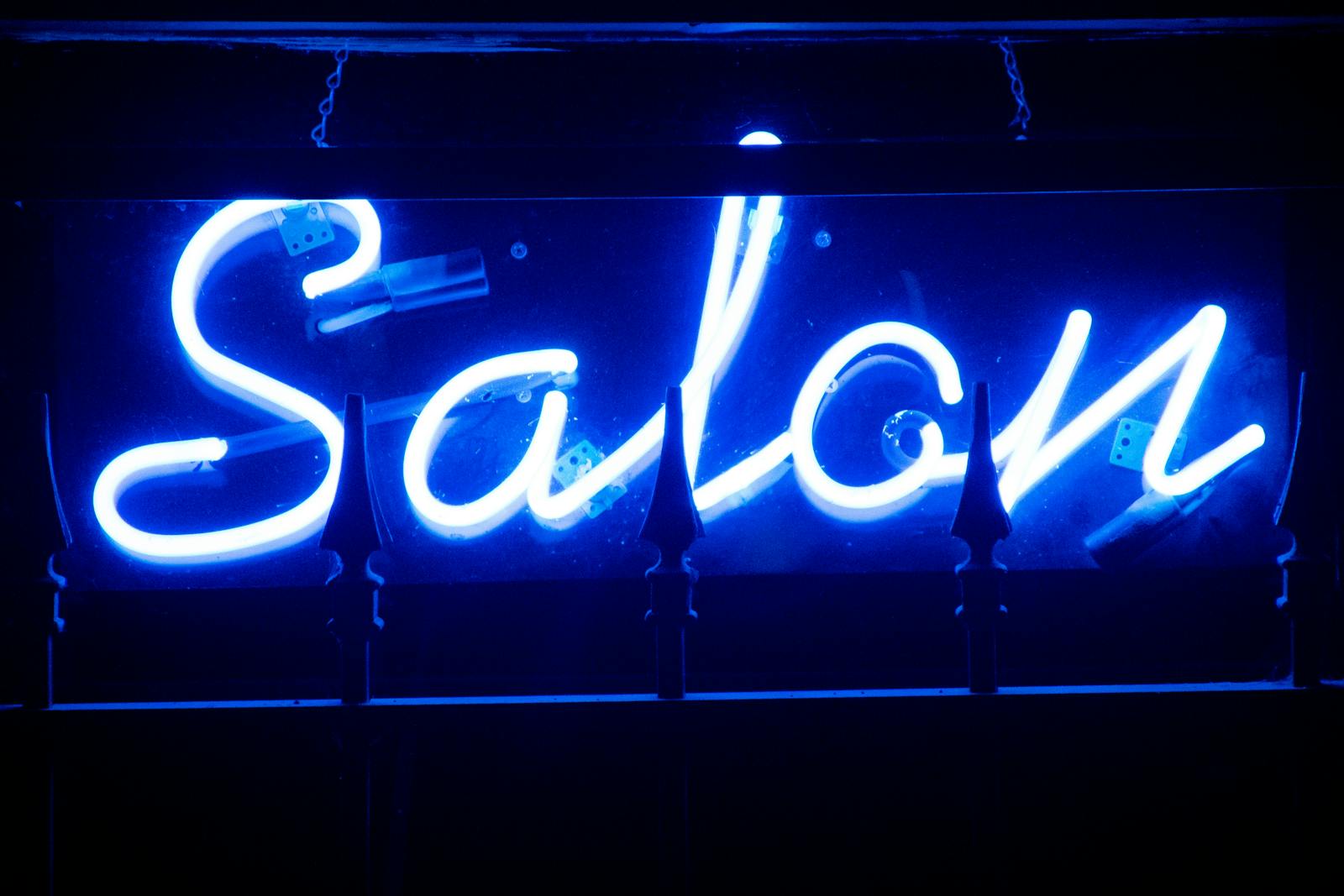 Vivid blue neon salon sign glowing brightly in the dark.